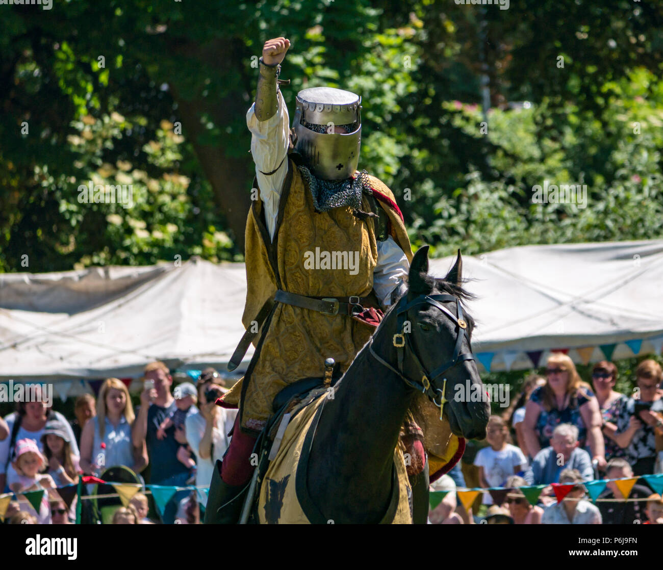 Jousting and Medieval Fair at Linlithgow Palace, Linlithgow, Scotland, United Kingdom, 30th June 2018. Historic Environment Scotland kick off their summer entertainment programme with a fabulous display of Medieval jousting in the grounds of the historic castle. The jousting is performed by Les Amis D'Onno equine stunt team. A knight raises his arm in salute to the crowd Stock Photo