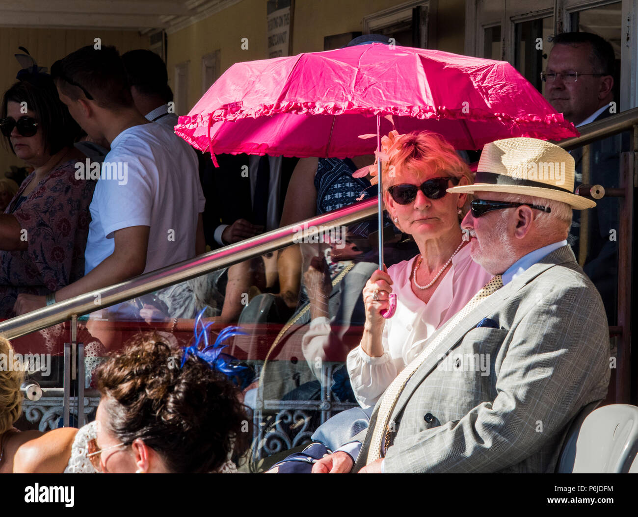 A lady and a gentleman shelter from the sunshine at York Racecourse, holding pink umbrella, York, England, 30th June 2018 Stock Photo