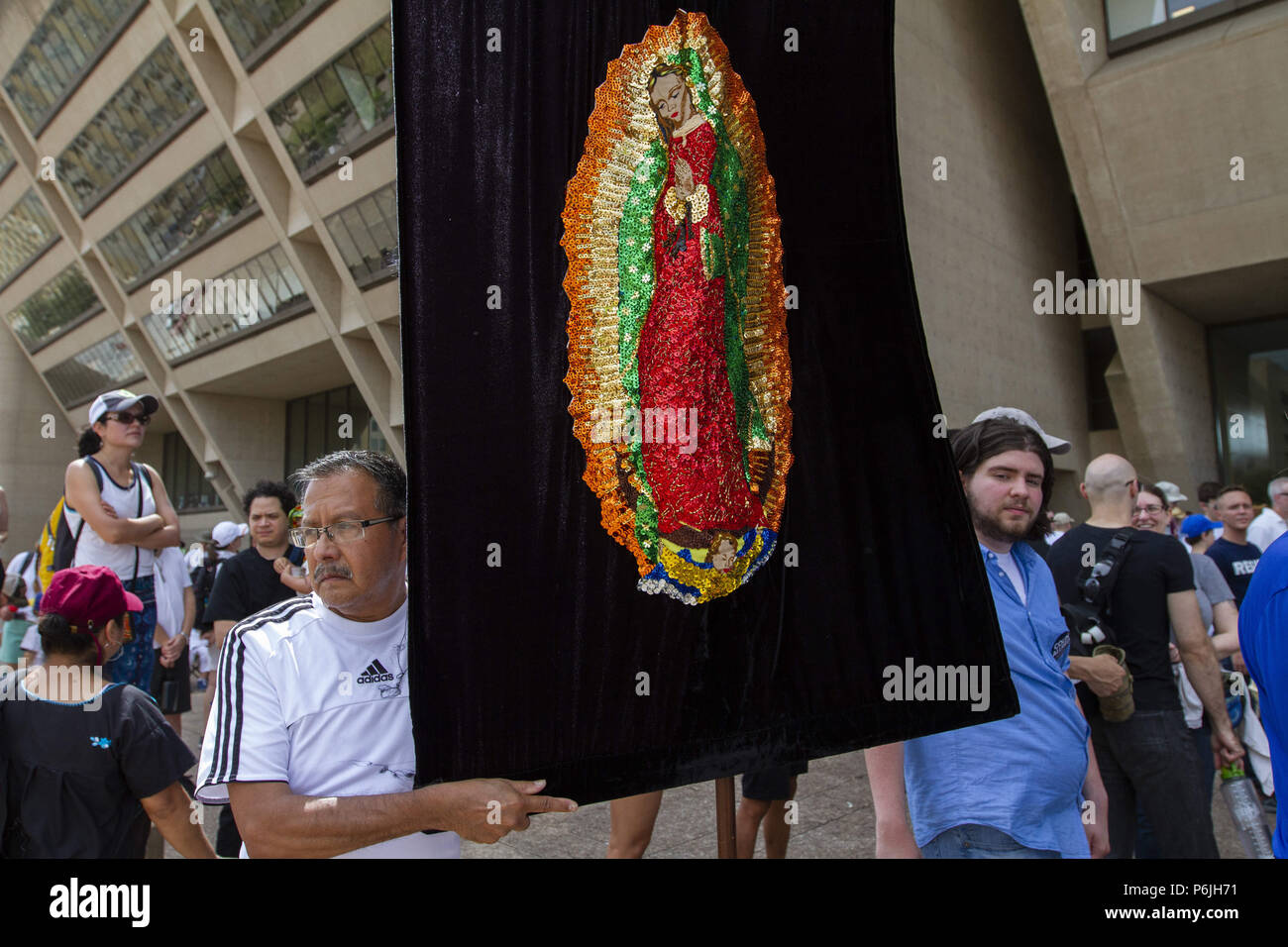 Dallas, Texas, USA. 30th June, 2018. Daniel Alvarado of Dallas stands next to the image of the Virgin of Gualdaupe he made during the Families Belong Together rally in front of of City Hall in downtown Dallas.Asked about the image, Alvarado responded ;''It's the standard bearer. It's a symbol. What's going on is horrific. It's time to vote and get ornanized. Credit: Jaime R. Carrero/ZUMA Wire/Alamy Live News Stock Photo