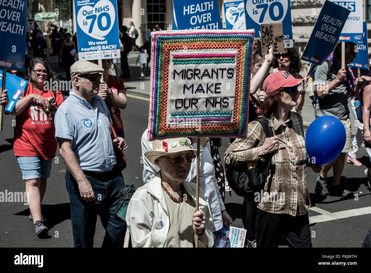 An old woman is seen carrying a poster during the demonstration. Tens of thousands of people marched during the hot Saturday weather through London to celebrate and demonstrate over Britain's National Health Service (NHS), ahead of its 70th birthday next week. Stock Photo