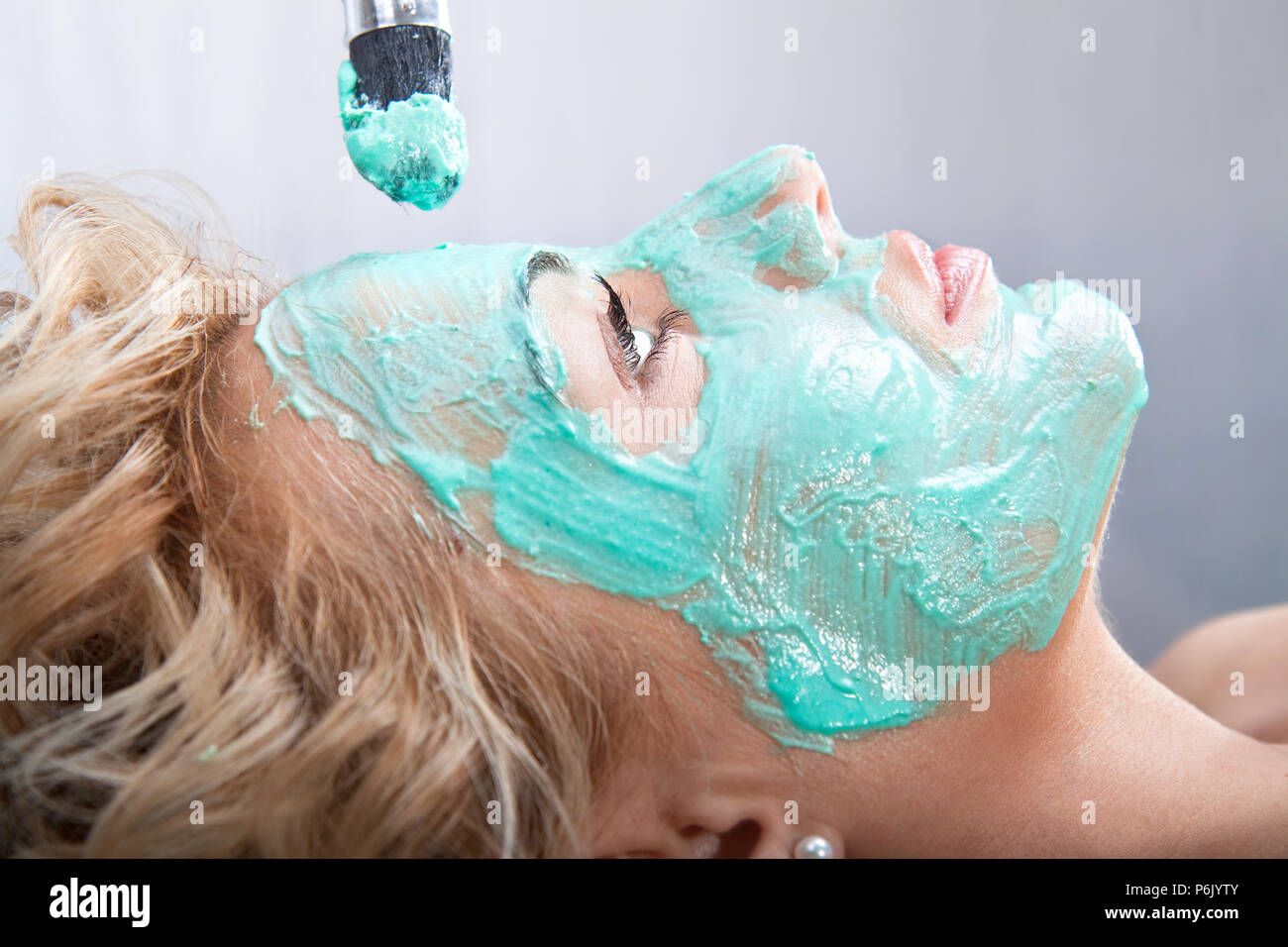 Applying mud face pack on woman face with brush Stock Photo
