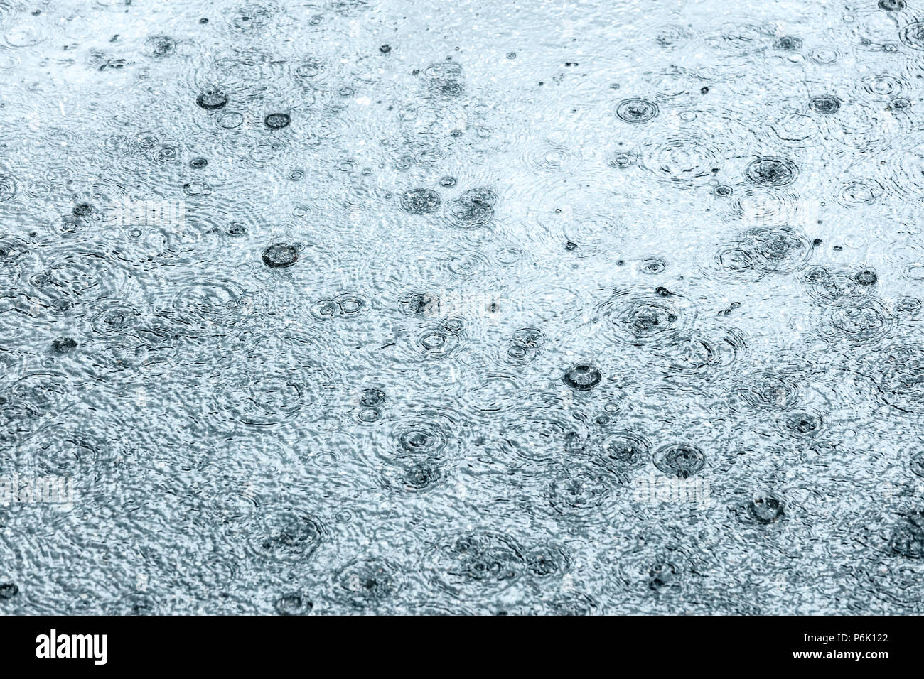 raindrops falling on flooded asphalt road creating bubbles Stock Photo