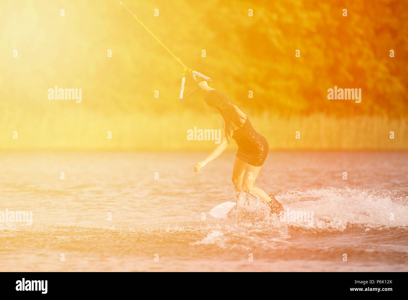Young pretty slim brunette woman riding wakeboard in a summer lake Stock Photo