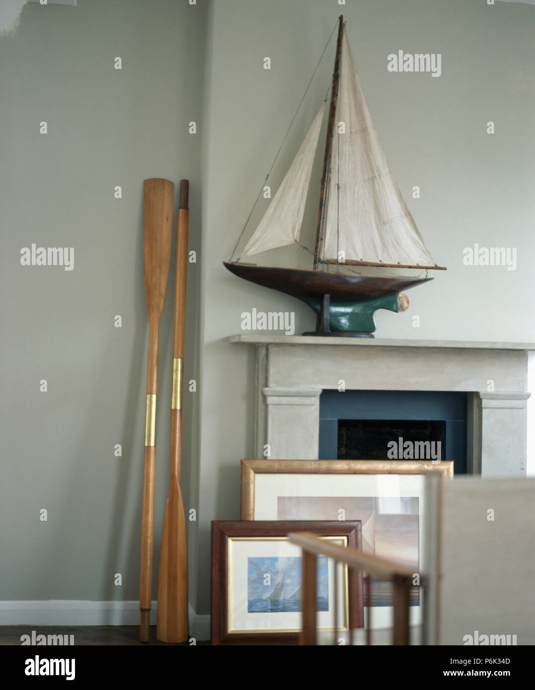 Still-Life of model sailing boat on mantelpiece beside wooden oars Stock Photo