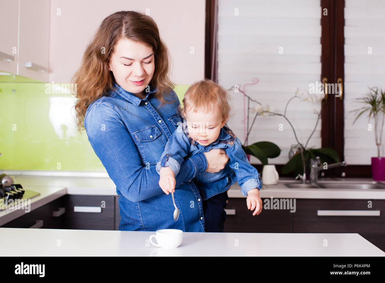 Cute little baby trying to stirr coffee in the arms of his mother Stock Photo