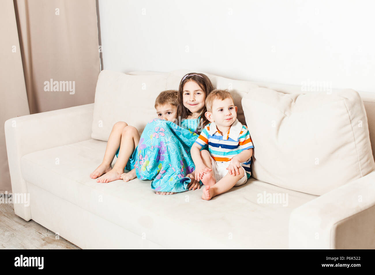 Three children are photographed sitting on the couch Stock Photo - Alamy