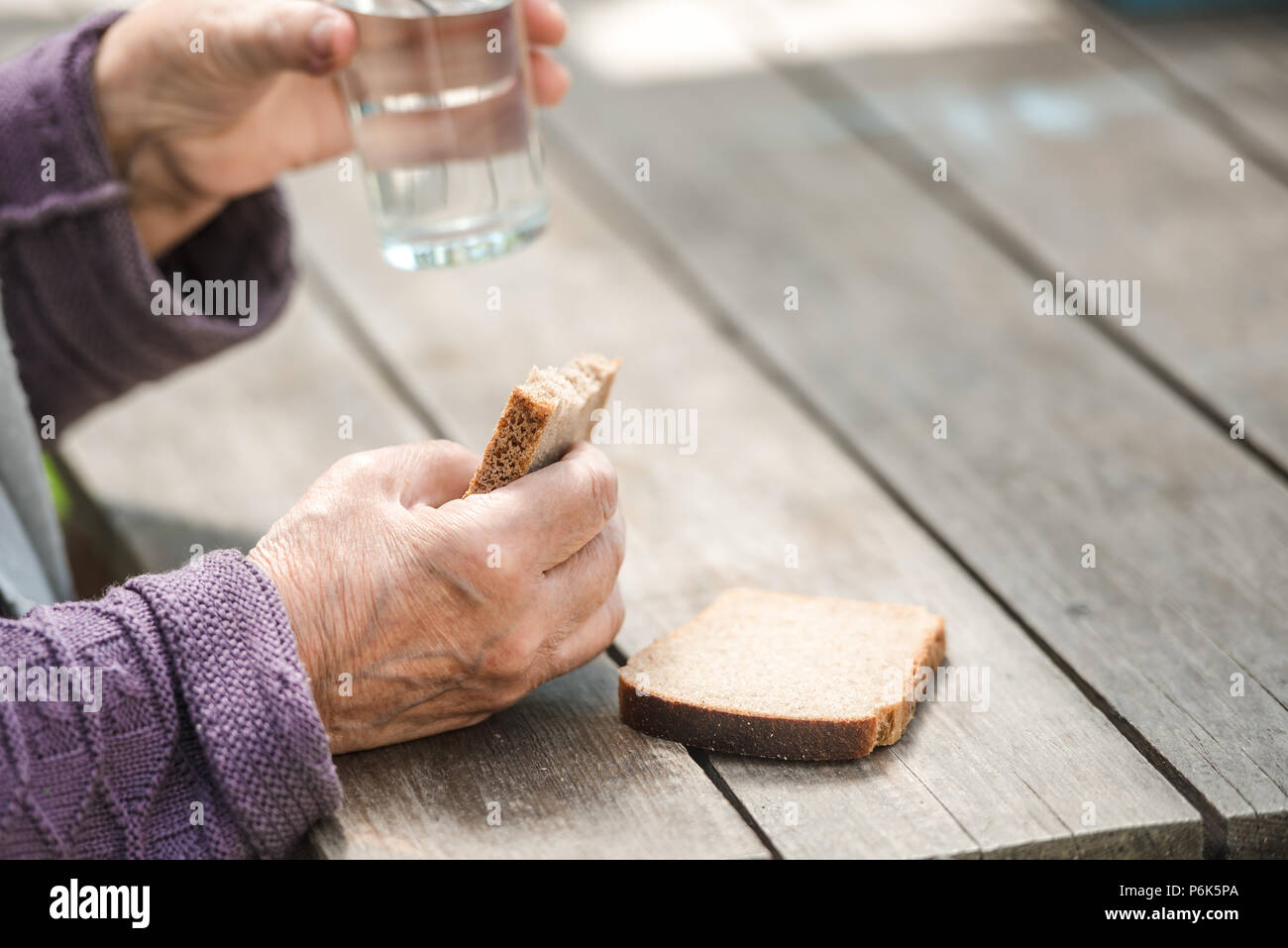 The old woman drinks water and eats bread at an old wooden table in a ...