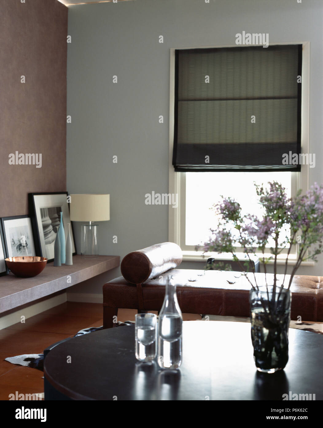 Grey Roman blind on window brown leather daybed in modern dining room Stock Photo