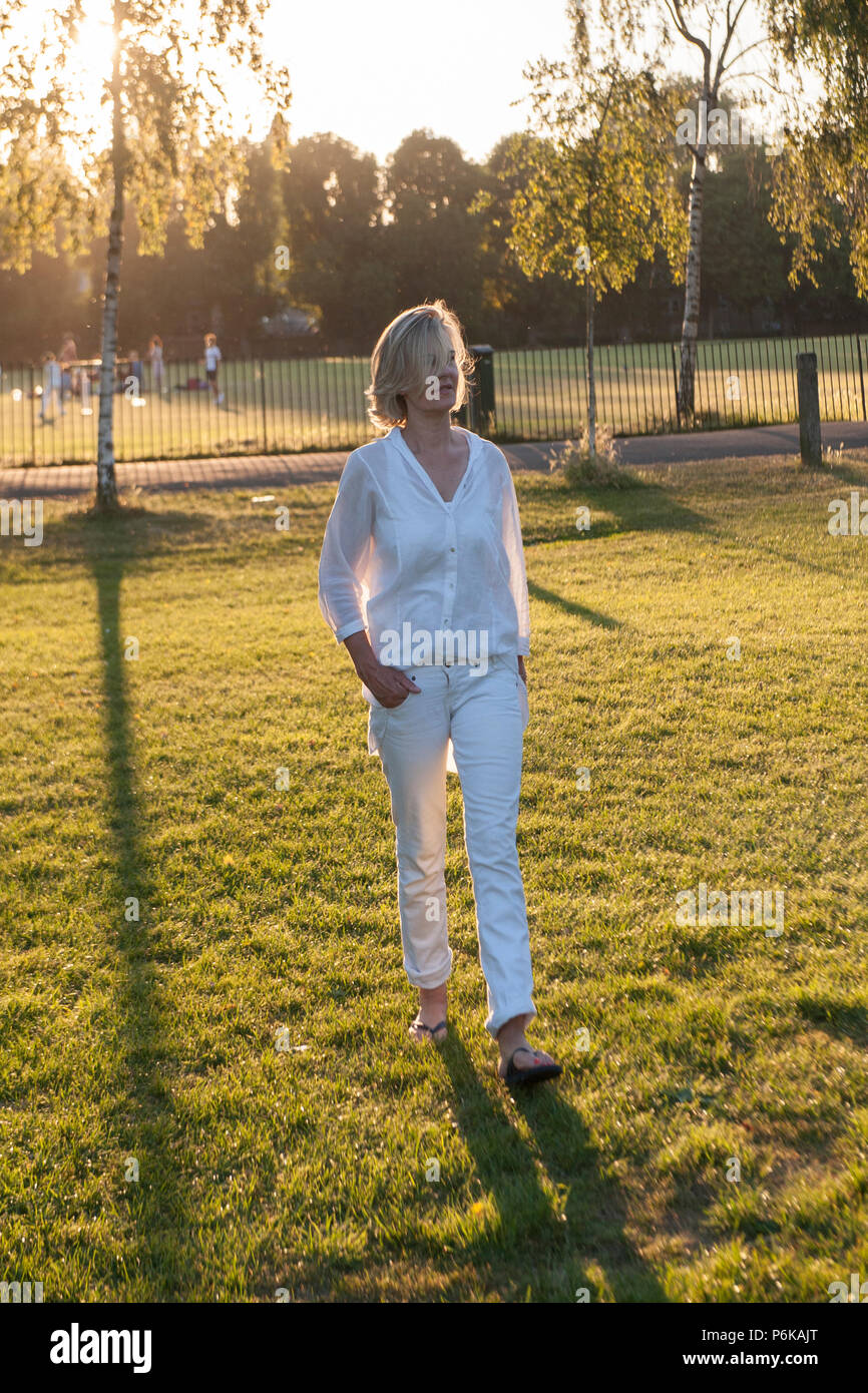 An attractive woman walks her dog in the late afternoon in a London park Stock Photo