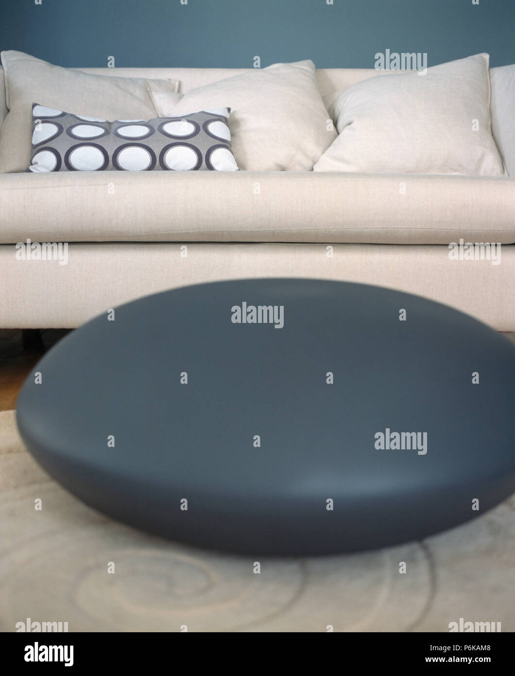 https://c8.alamy.com/comp/P6KAM8/close-up-of-circular-dark-grey-leather-cushion-in-front-of-cream-sofa-with-matching-cushions-P6KAM8.jpg