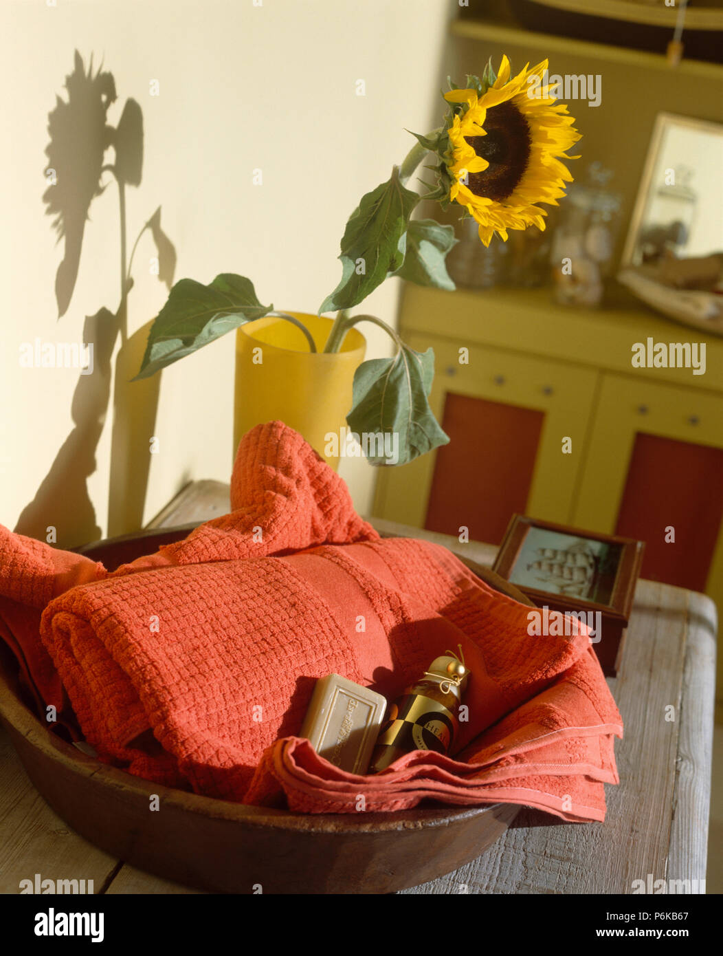 Close-up of salmon-pink towl in bowl on table with single sunflower in yellow vase Stock Photo