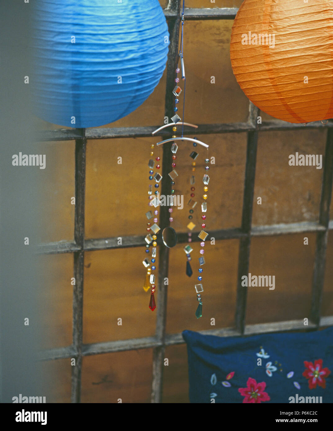 Close-up of blue and orange paper lampshades and glass mobile on old metal windowframe Stock Photo