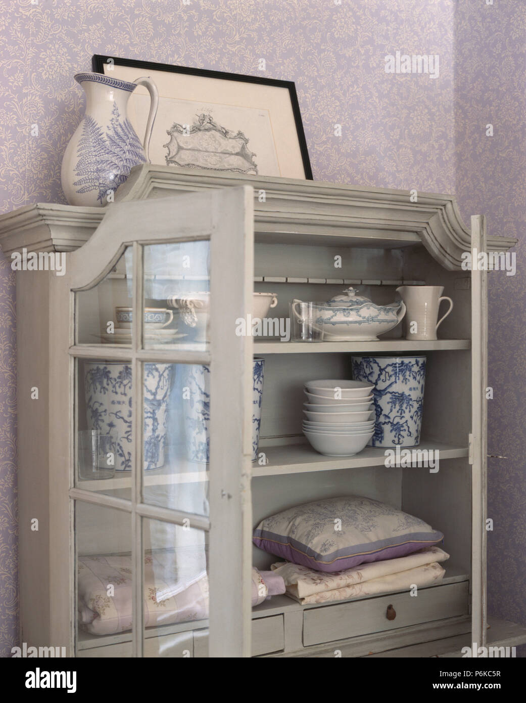 Close Up Of Glass Fronted Pale Grey Cupboard With Bowls And Vases