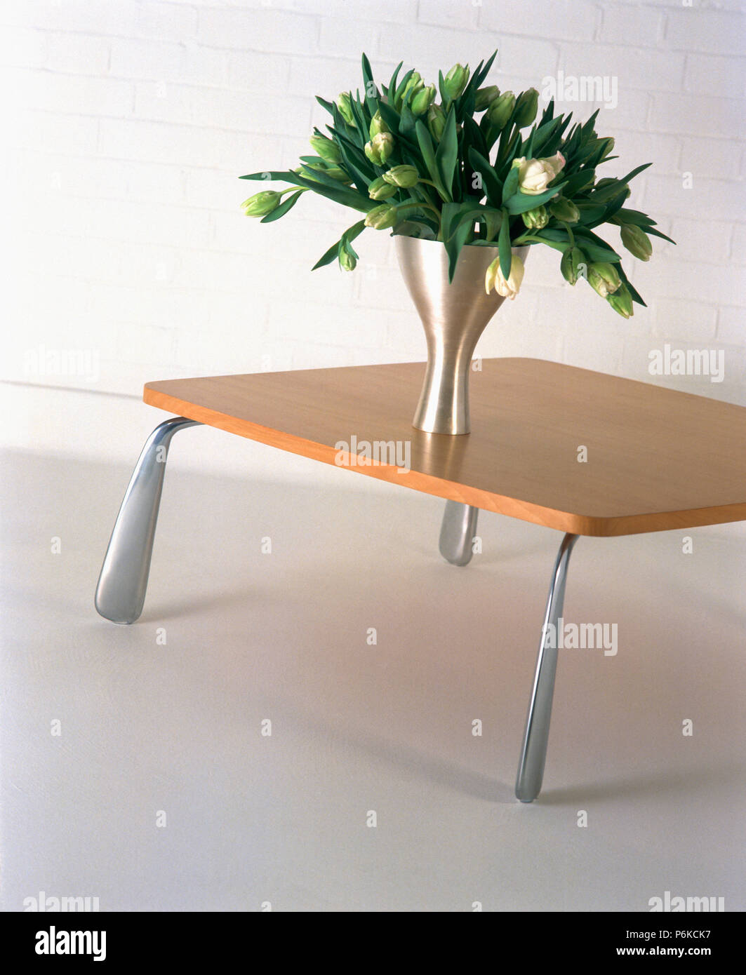 Closeup of metal vase of lilies on pale wood modern table with metal