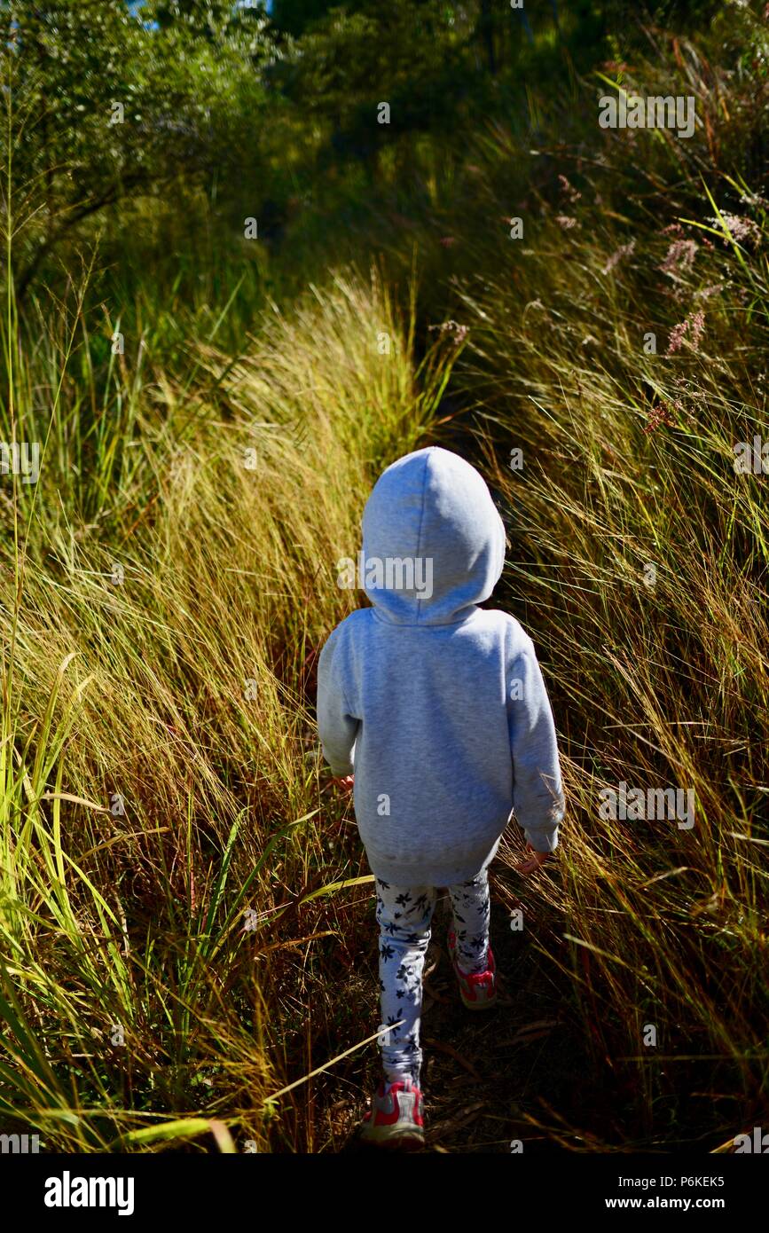 Small child walking through long grass with grey hoodie hires stock