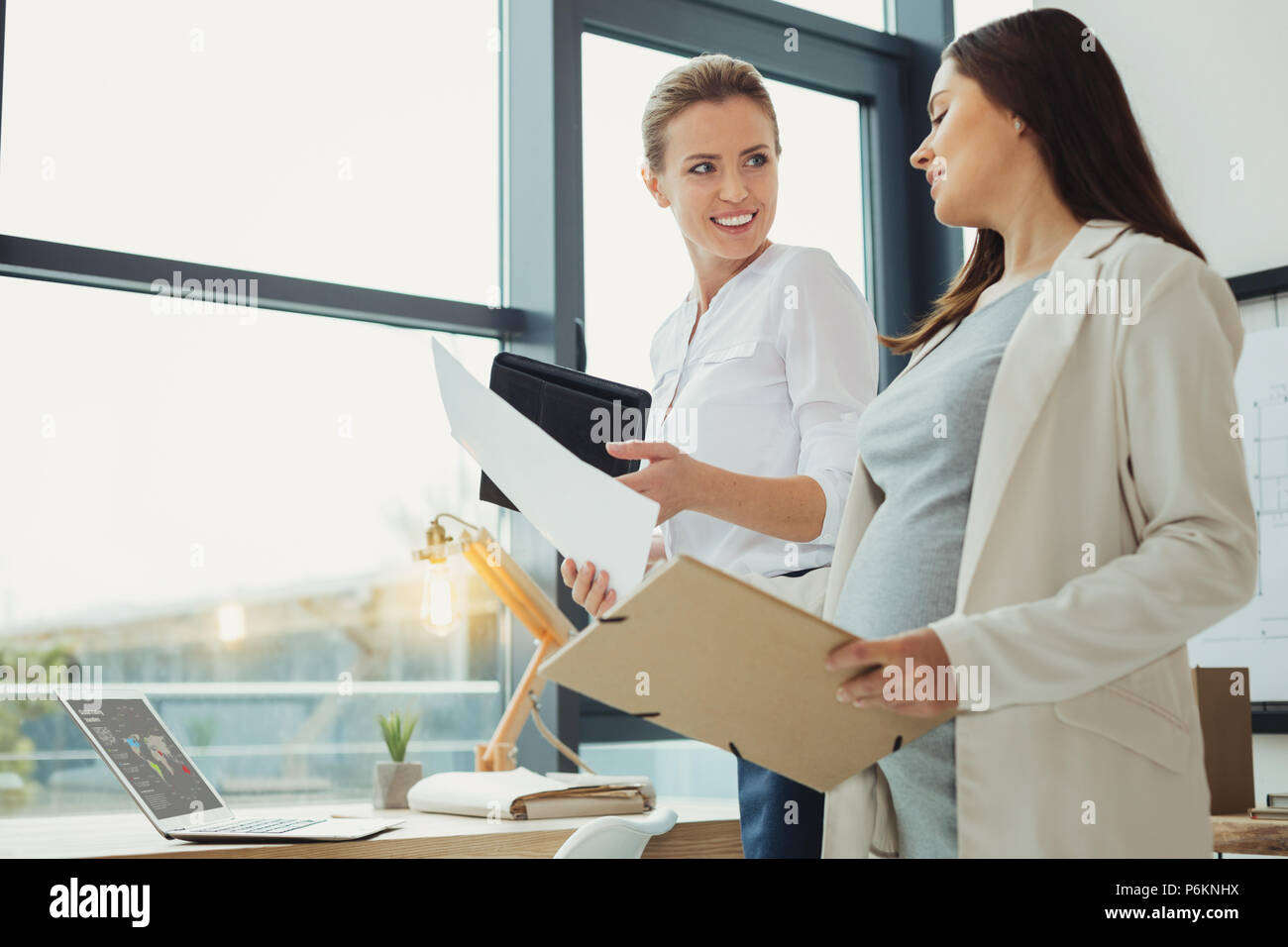 Pregnant worker holding a document while showing it to a cheerful boss Stock Photo