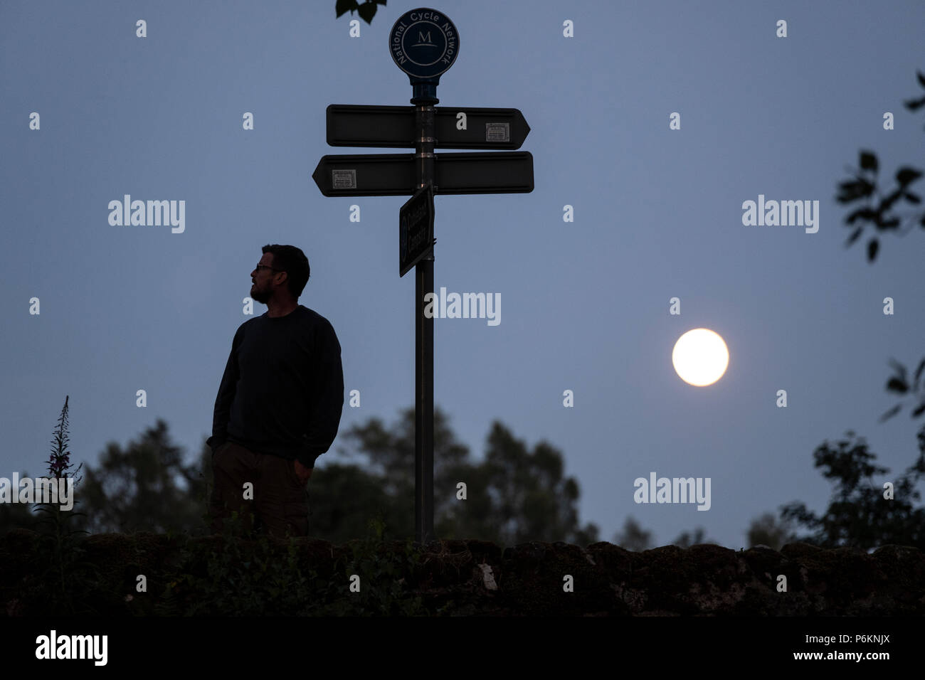 A man pauses to view a road sign in the moonlight near Dunmuck in the Scottish Highlands. Stock Photo