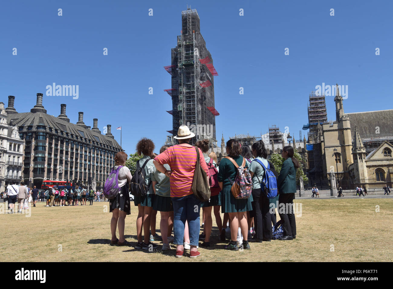 Tourists and visitors to London gather in groups in Westminster outside the Houses of Parliament where Big Ben is covered in scaffold as it undergoes  Stock Photo