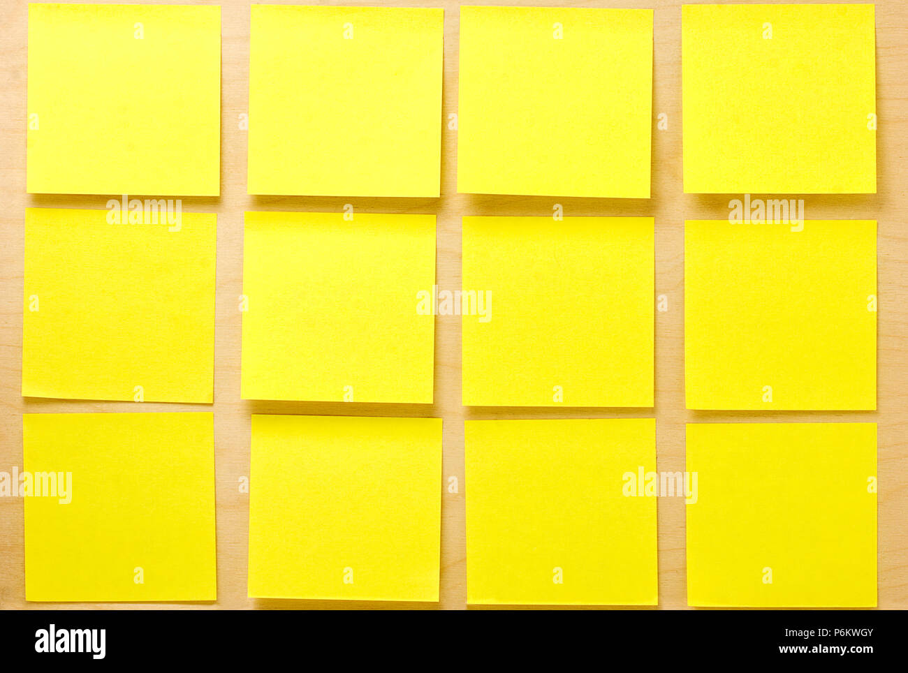 Blank well-ordered square yellow postit notes affixed on a wooden board Stock Photo