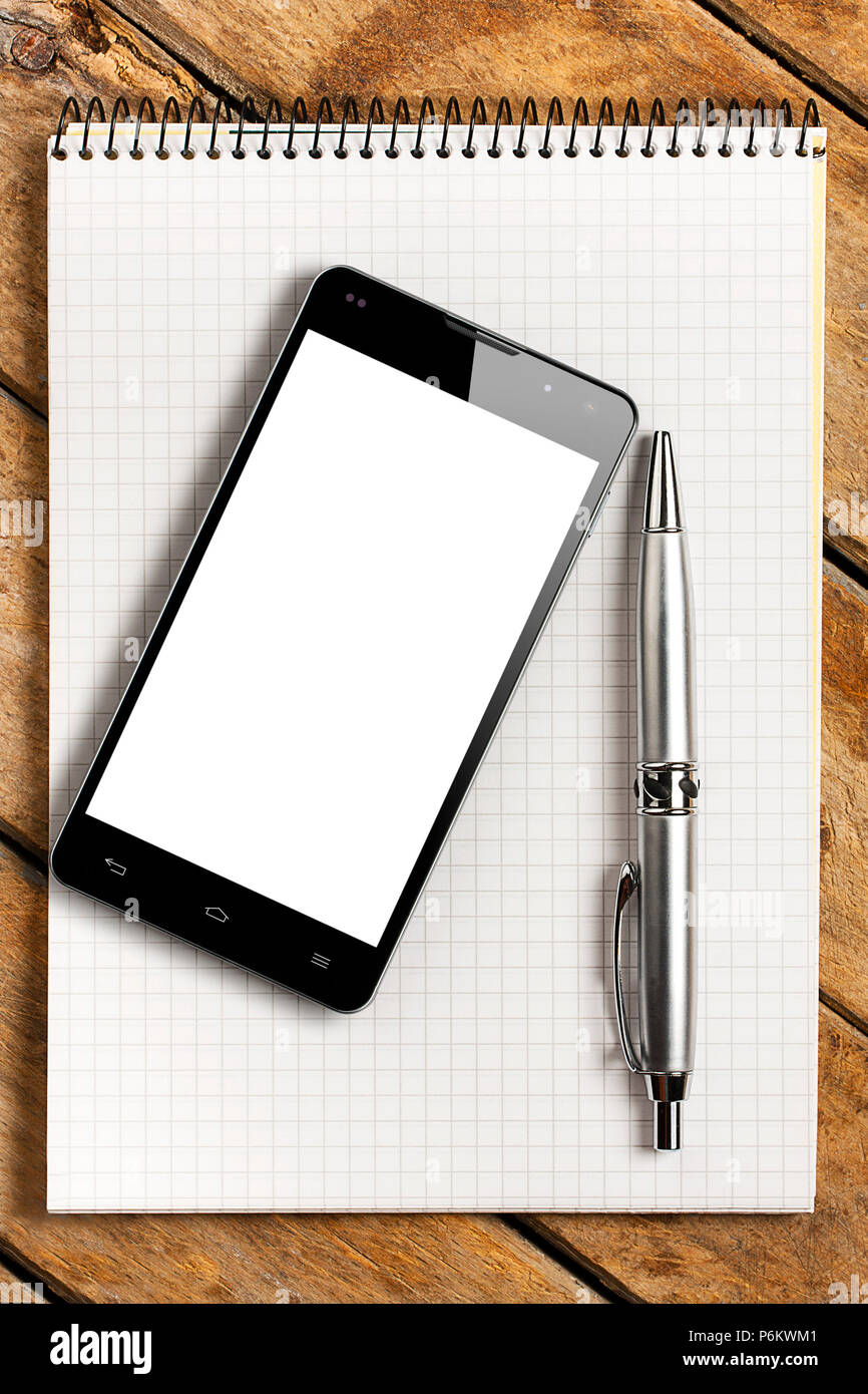 Smartphone with blank white screen and silver pen on a white spiral squared notebook on rustic wooden table Stock Photo