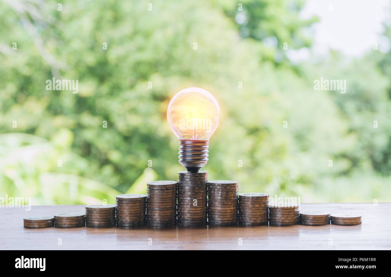 Energy saving light bulb and tree growing on stacks of coins on nature ...