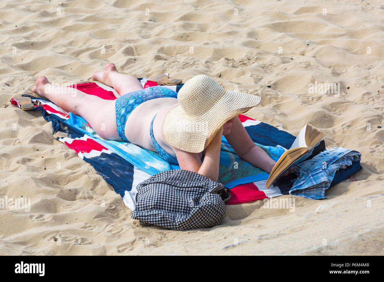 Bournemouth, Dorset, UK. 1st July 2018. UK weather: hazy sunshine, but still warm as thousands of sunseekers head to the beaches at Bournemouth to enjoy a day at the seaside. woman sunbathing on beach reading book wearing floppy hat. Credit: Carolyn Jenkins/Alamy Live News Stock Photo