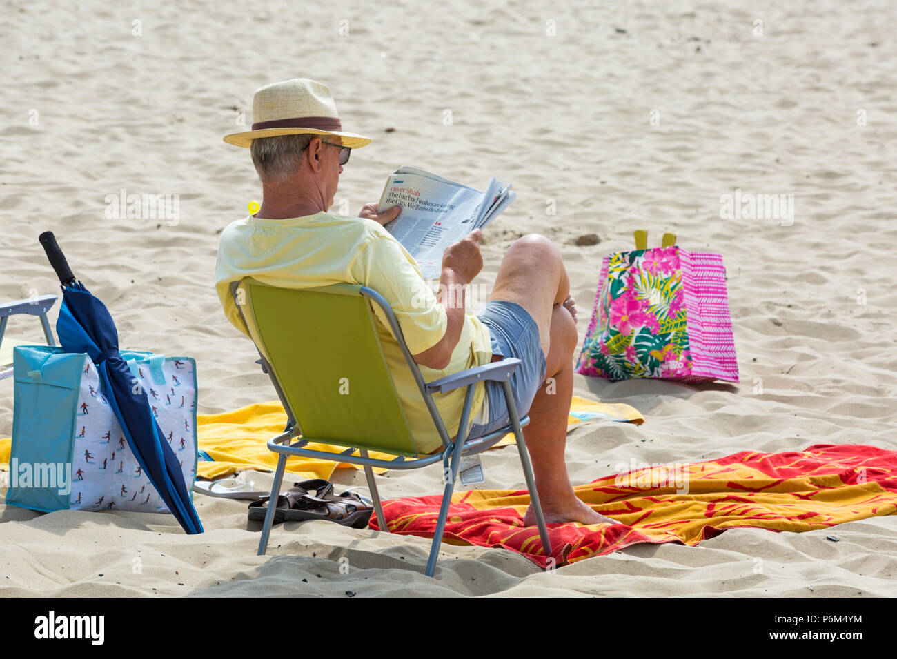 Bournemouth, Dorset, UK. 1st July 2018. UK weather: hazy sunshine, but still warm as thousands of sunseekers head to the beaches at Bournemouth to enjoy a day at the seaside. Prepared for all weathers! Man sitting in chair reading the Sunday Times newspaper. Credit: Carolyn Jenkins/Alamy Live News Stock Photo