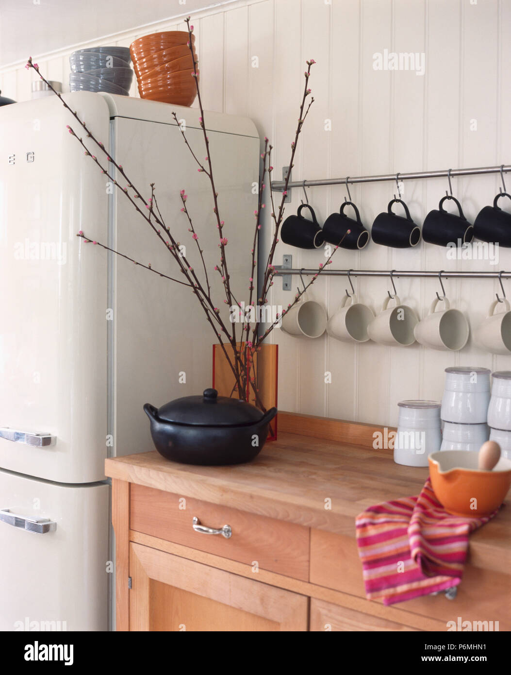 Black and white cups on metal storage rack above freestanding cupboard beside tall Smeg fridge-freezer Stock Photo