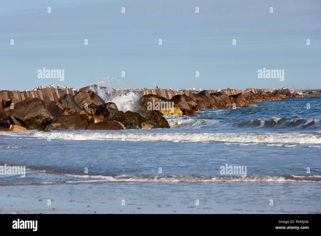 Waves crashing against a breakwall lined with sea birds Stock Photo