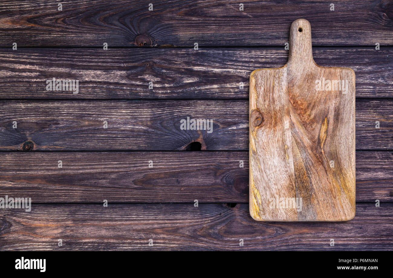 Old cutting board on dark wooden table. Top view. Copy space Stock