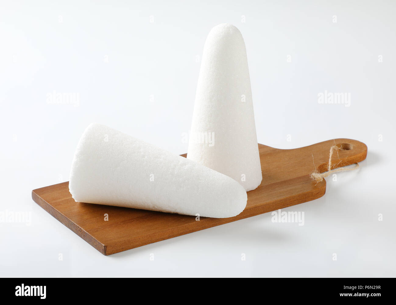 two white sugar loaves or cones on wooden cutting board Stock Photo