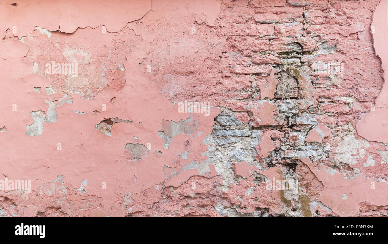 Full frame background of a weathered, damaged and plastered wall painted in pink. Plaster is partly peeled off revealing old bricks. Stock Photo