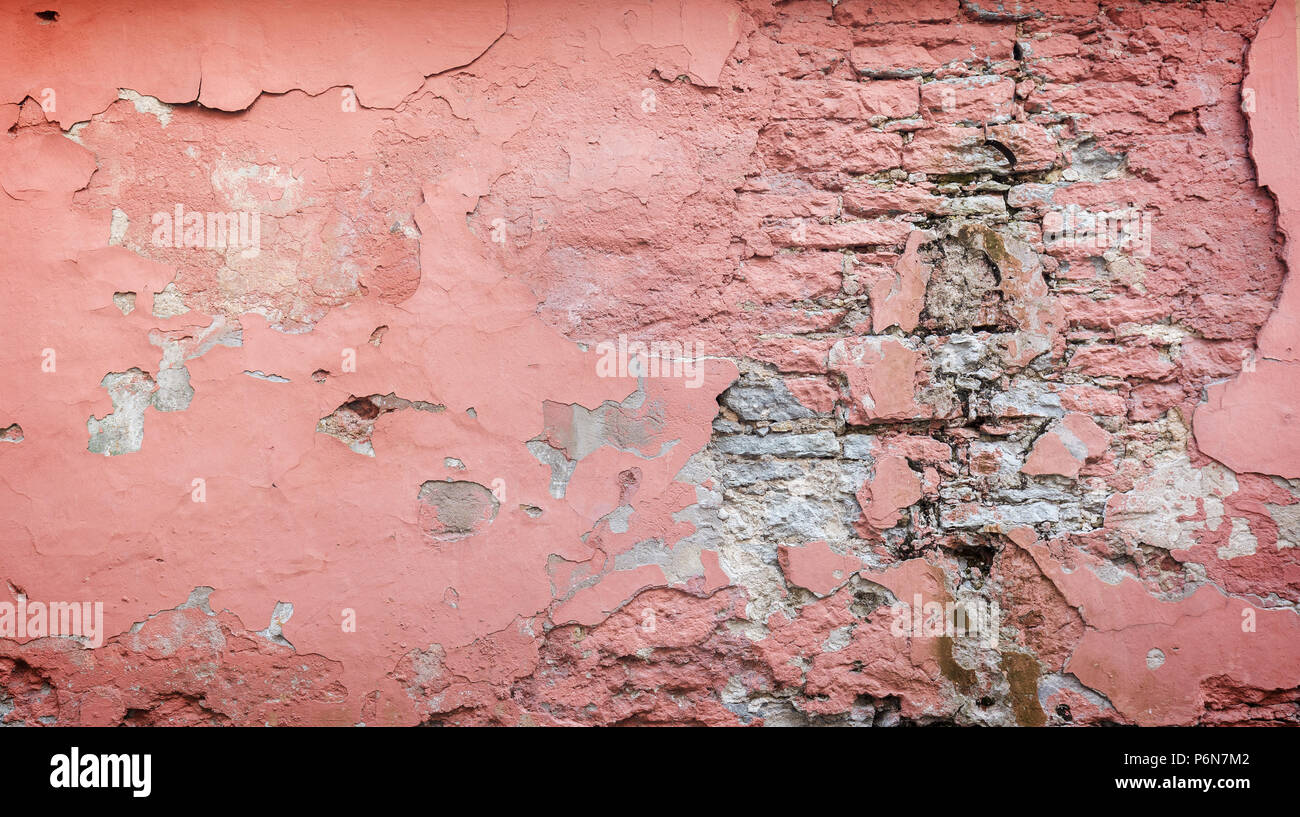 Full frame background of a weathered, damaged and plastered wall painted in pink. Plaster is partly peeled off revealing old bricks. Stock Photo