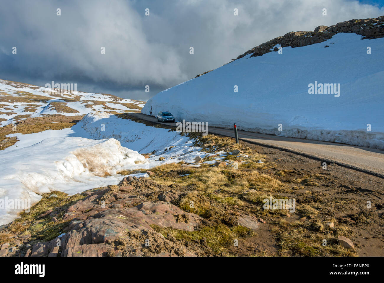 A car passing a large snow drift near the summit of the Bealach na Bà road, in the Applecross hills, Highland Region, Scotland, UK Stock Photo