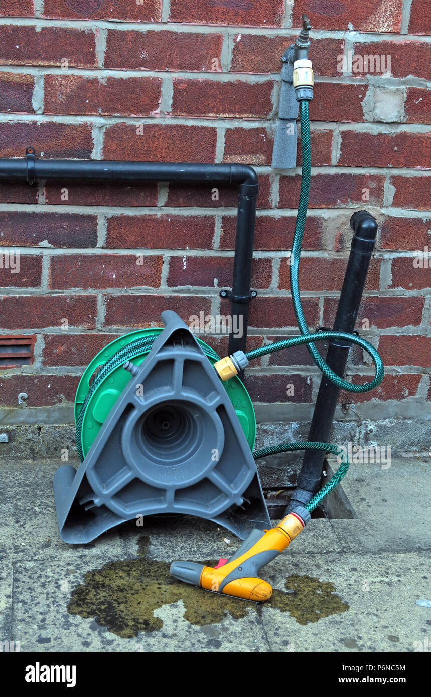 Hosepipe reel connected to a standpipe in garden, with leaking water Stock Photo