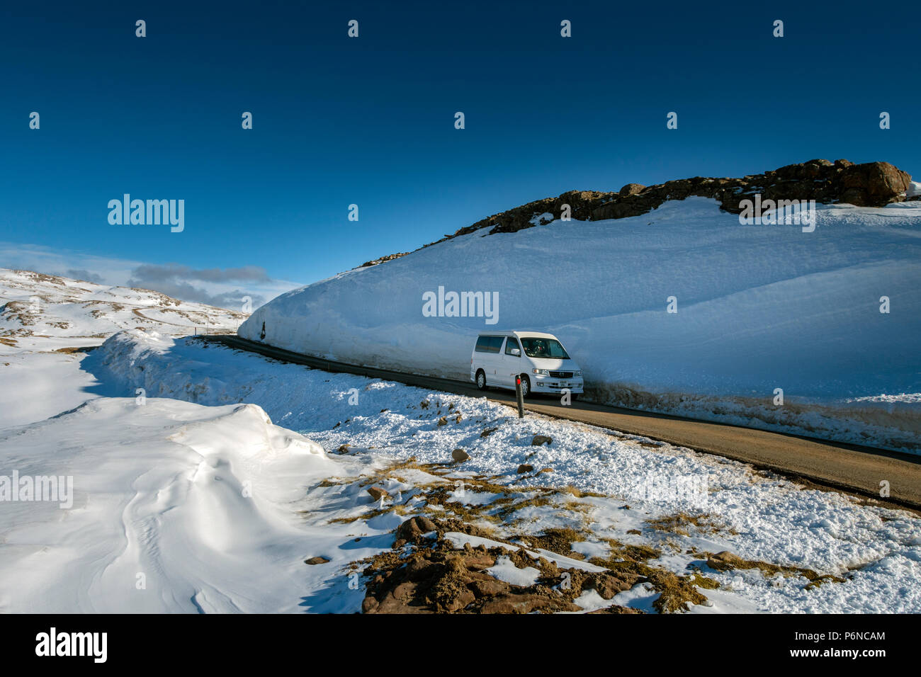 A Mazda Bongo campervan passing a large snow drift near the summit of the Bealach na Bà road, in the Applecross hills, Highland Region, Scotland, UK Stock Photo