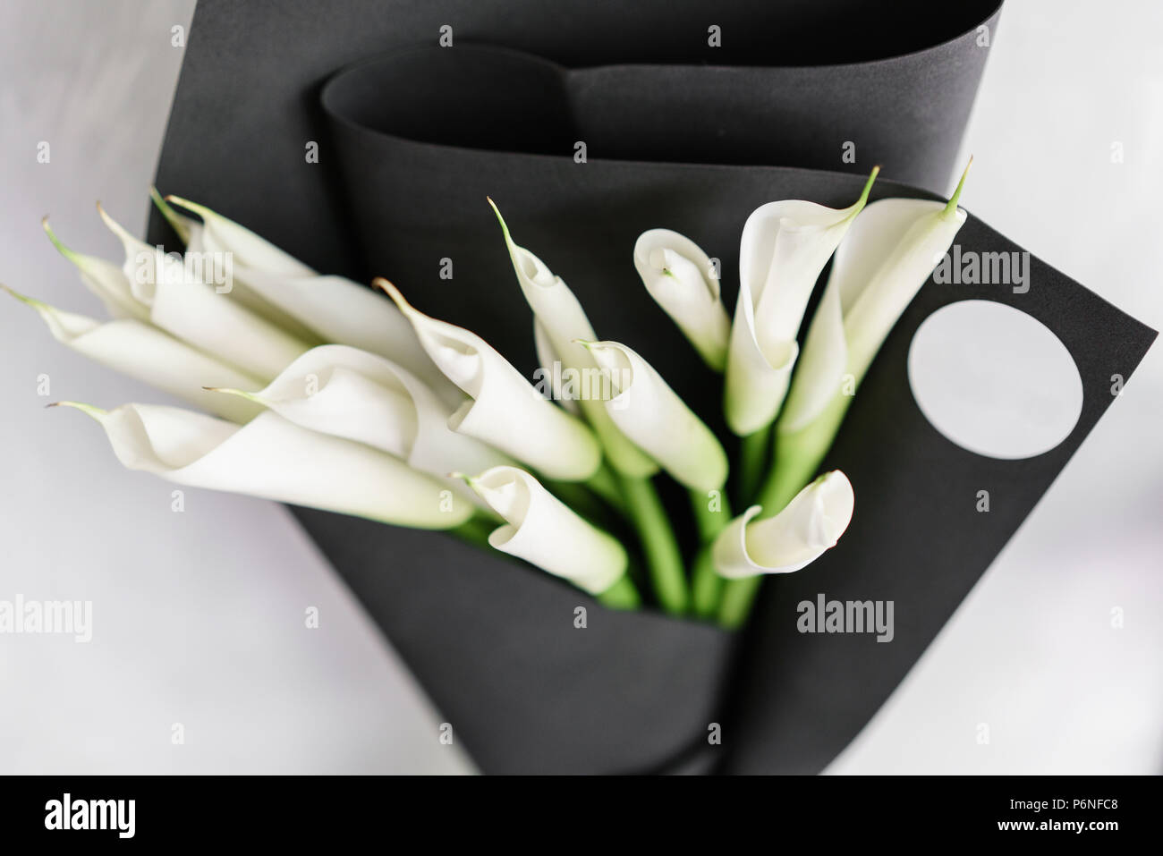 Beautiful white Calla lilies in glass vase on black paper cover Stock