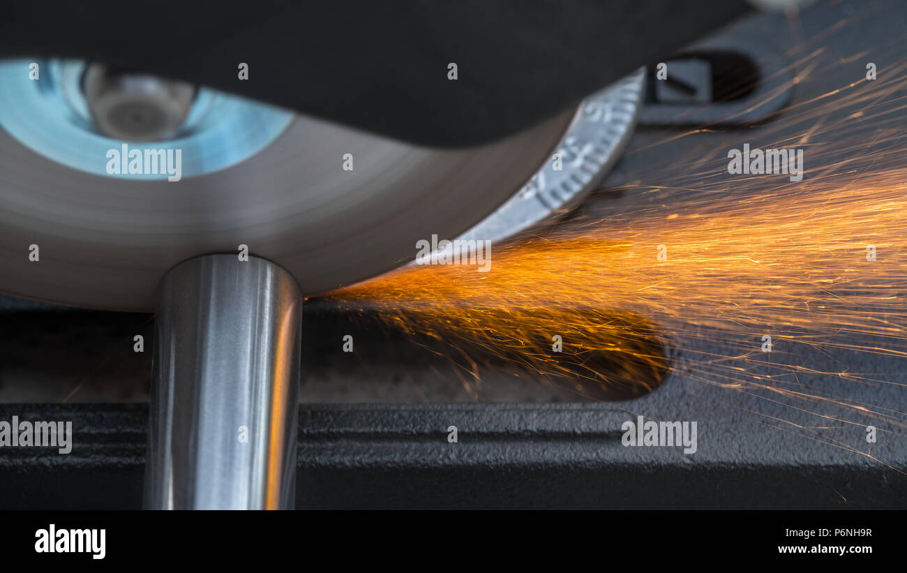 Cutting a metallic rod by a circular saw machine. Close-up of hot sparks when sawing a steel workpiece. Motion blur of disc with sharp blade. Stock Photo