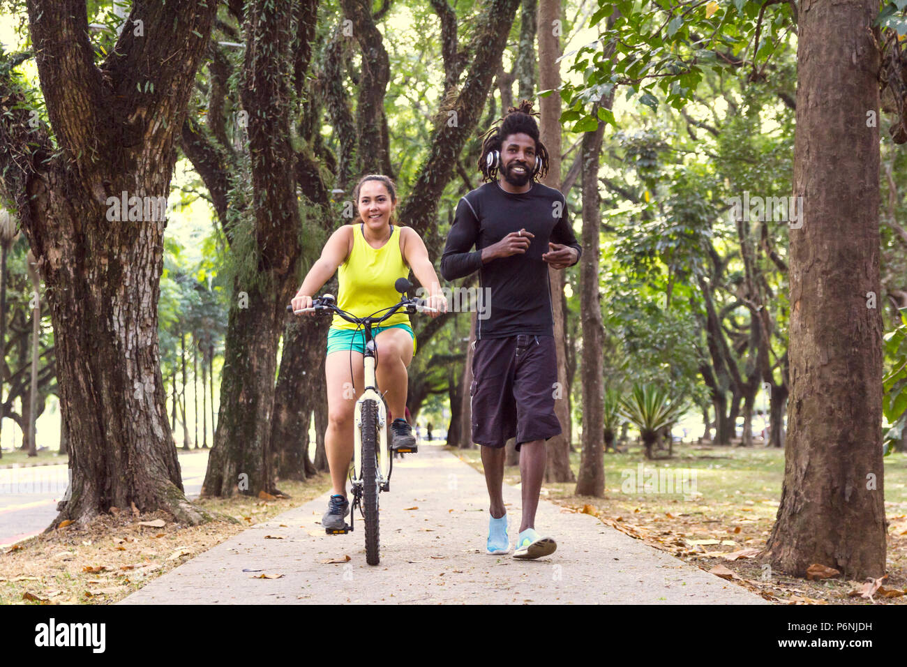 Woman is riding a bike next to man running in wooded street