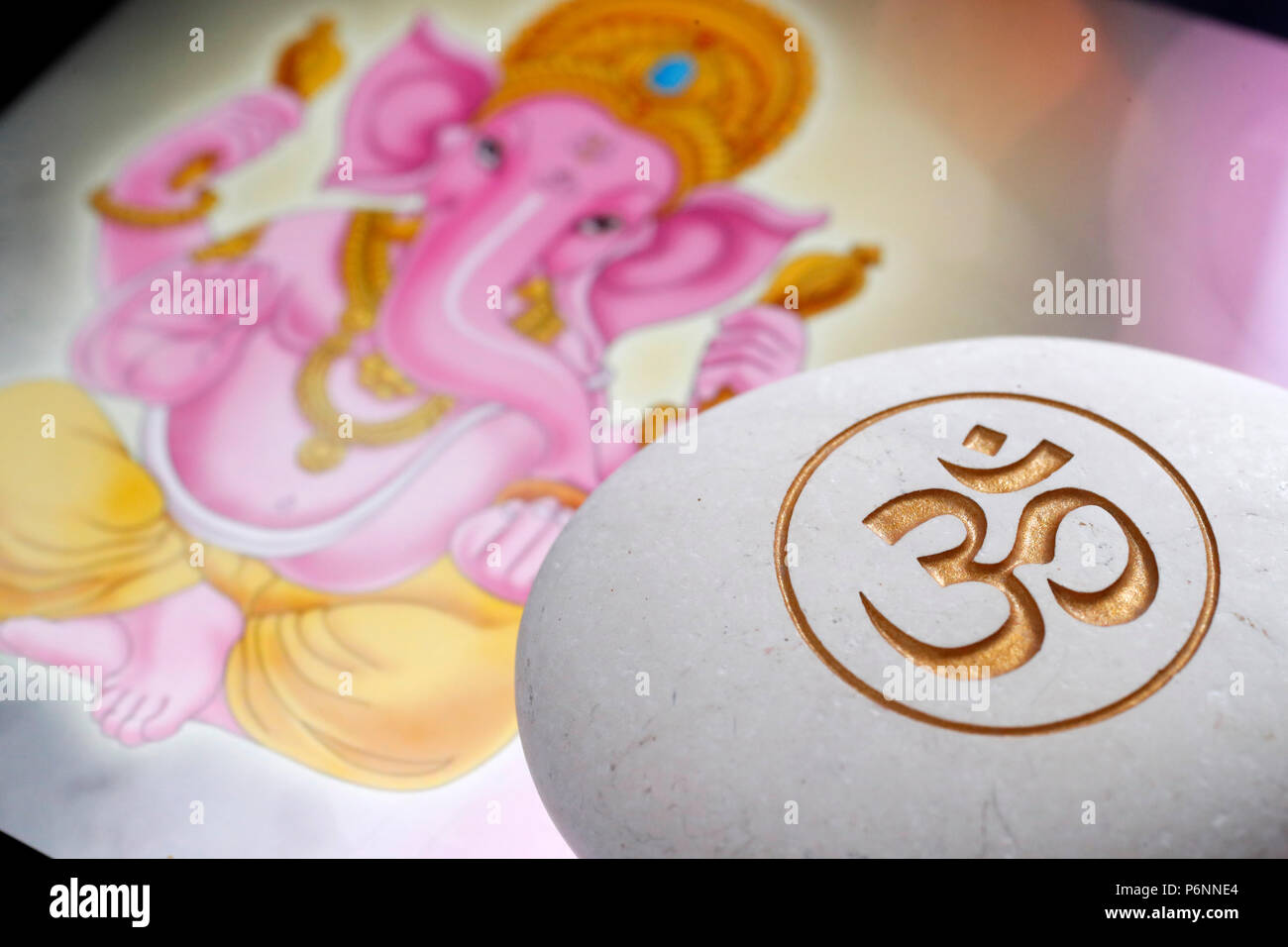 The Om or Aum symbol of Hinduism and Buddhism on a white stone.  Image of Ganesha also known as Ganapati on a tablet. Stock Photo