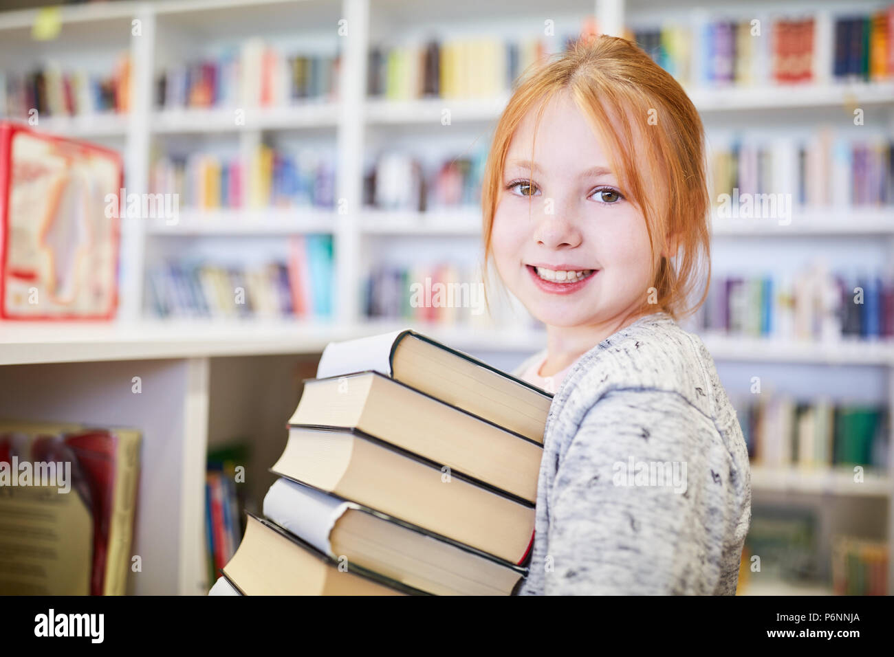 Smiling student with stack of books to borrow in the library of the school Stock Photo