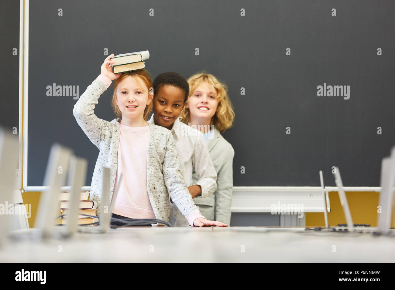 Three children as a pupil silly around in the multicultural school at the blackboard Stock Photo