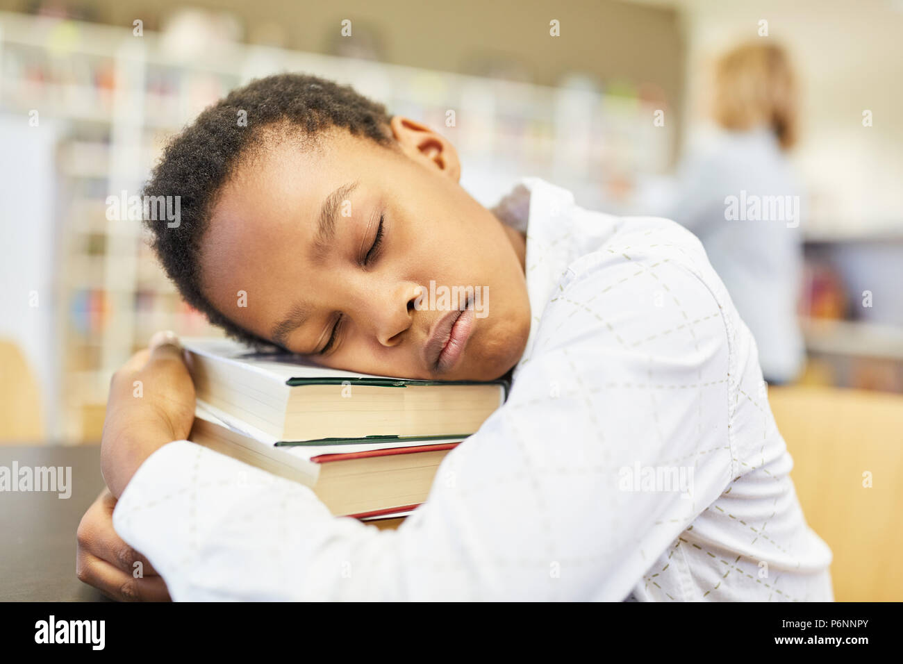 Sleeping boy as a pupil in the library with a big stack of books Stock Photo