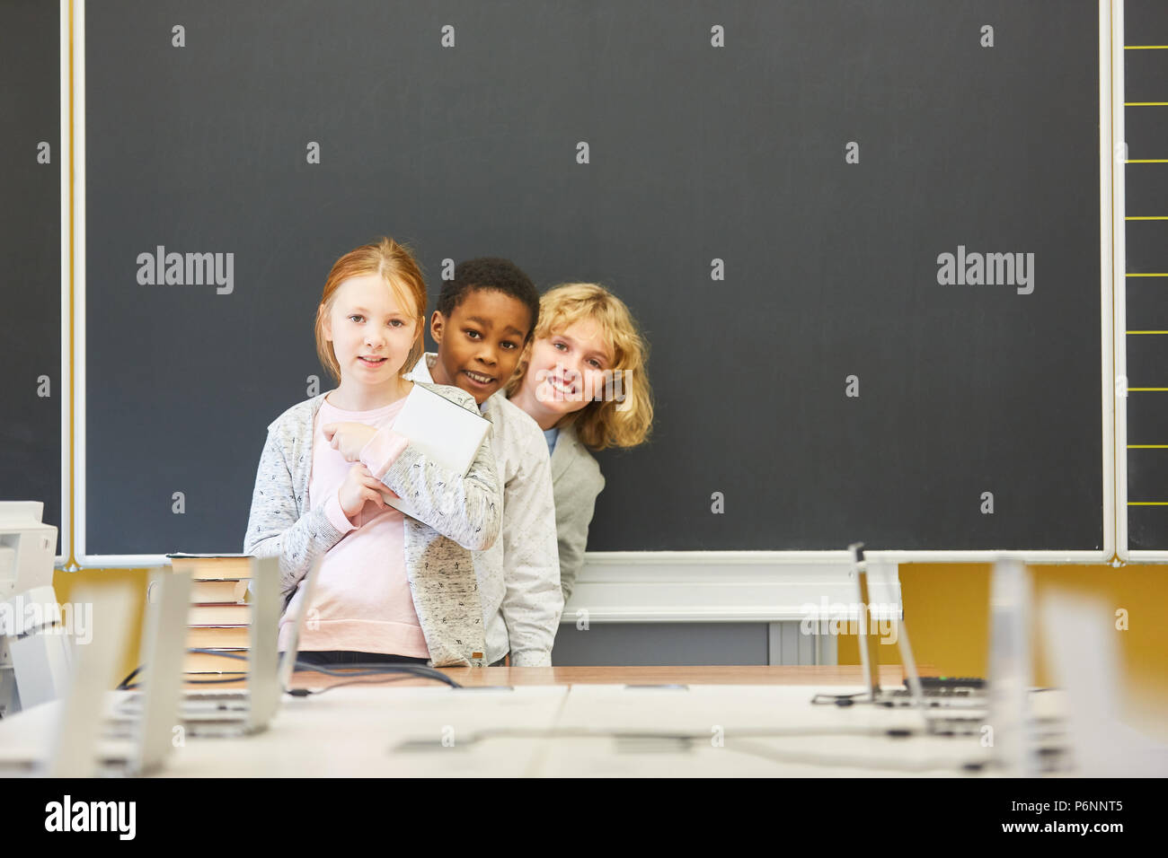 Three children in front of an empty blackboard in the multicultural elementary school Stock Photo