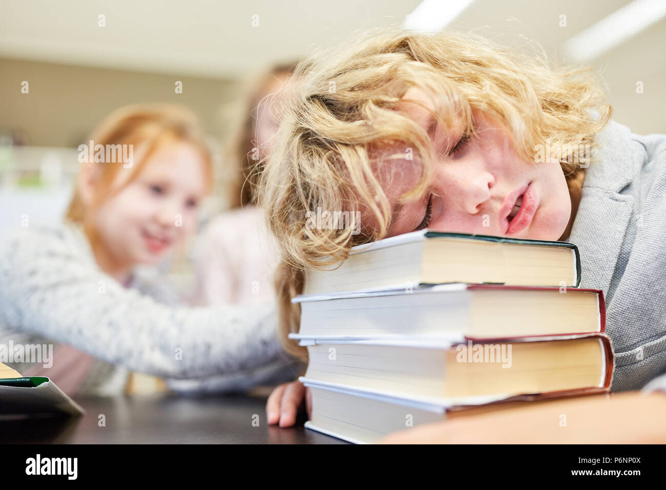Pupil sleeps exhausted with his head on a pile of books in class Stock Photo
