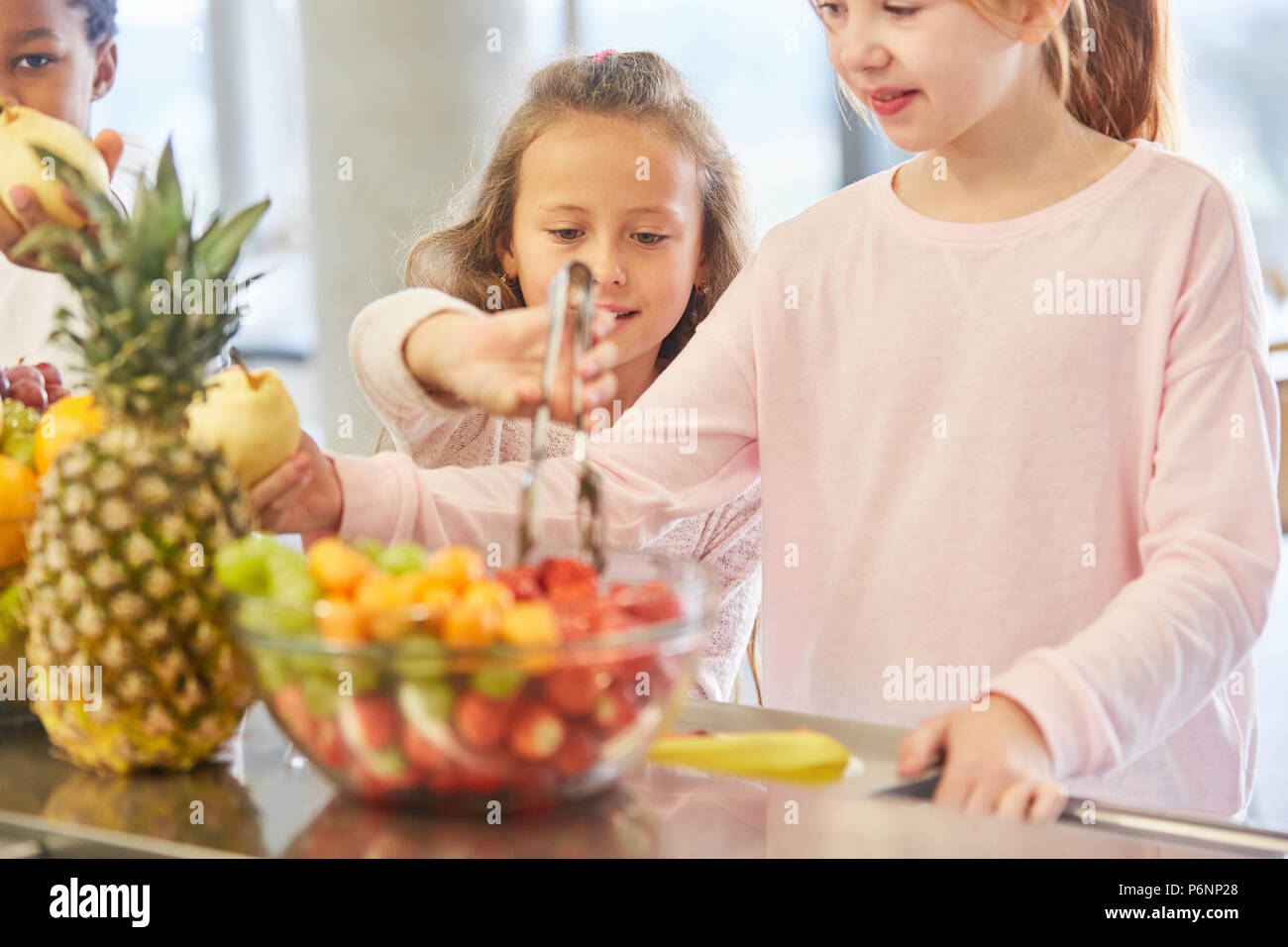 Girl at the fruit buffet of the kindergarten cafeteria take fresh fruit Stock Photo