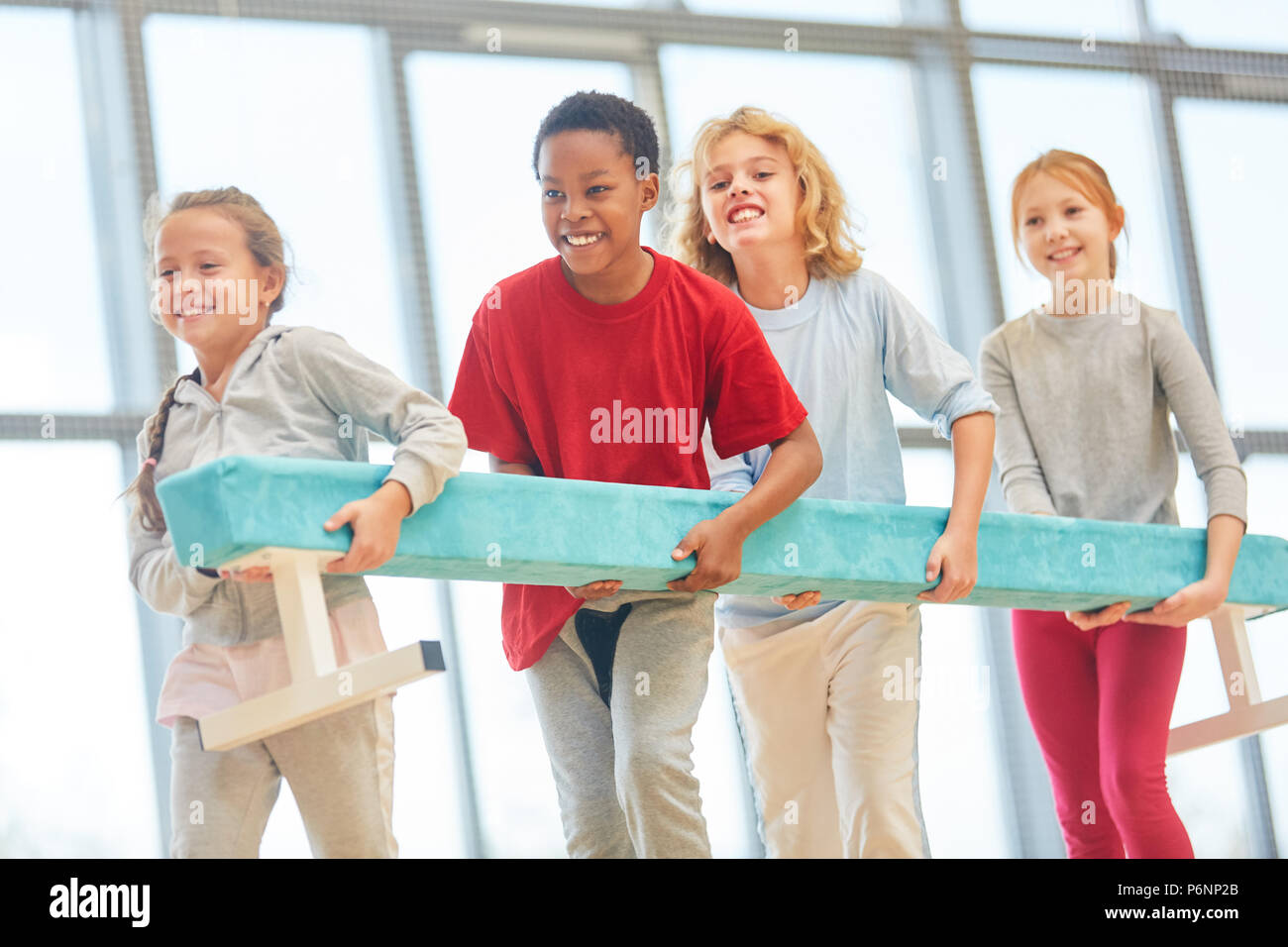 Happy children in physical education wear a balance beam as a team Stock Photo