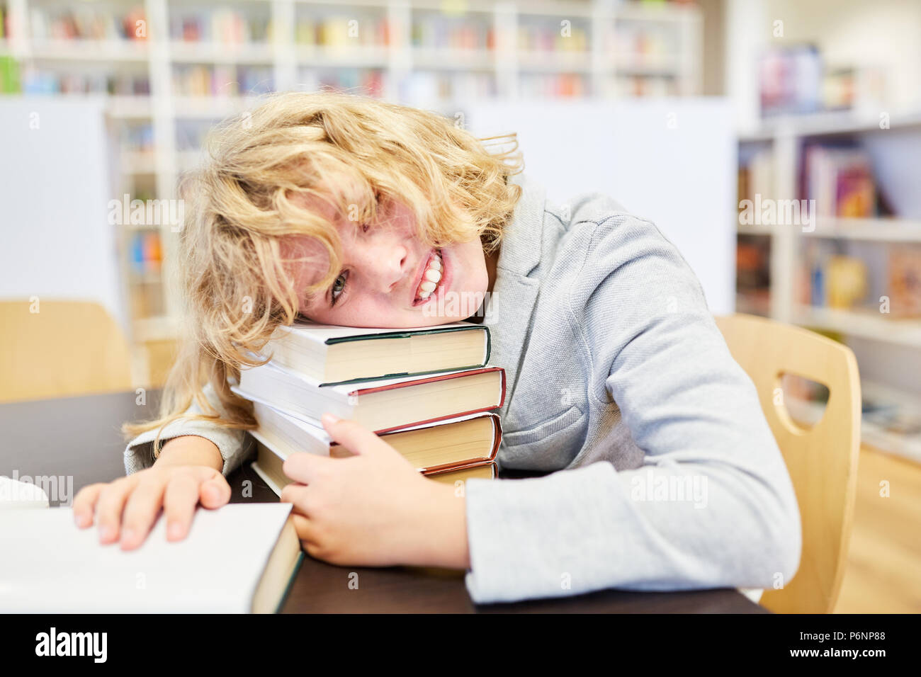 Happy boy as a pupil with many books in the library of the school Stock Photo