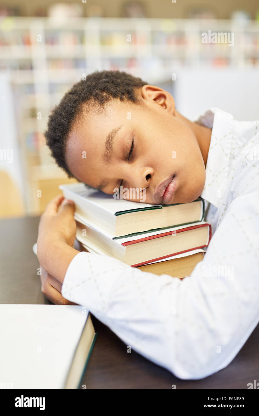 Pupil in the school library sleeps on a stack of books Stock Photo
