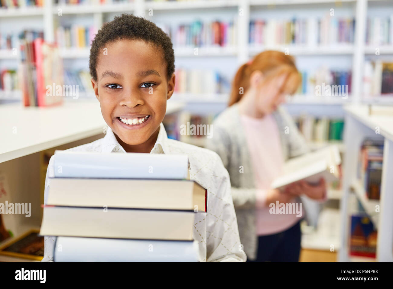 African schoolboy with a stack of books in the library of elementary school Stock Photo